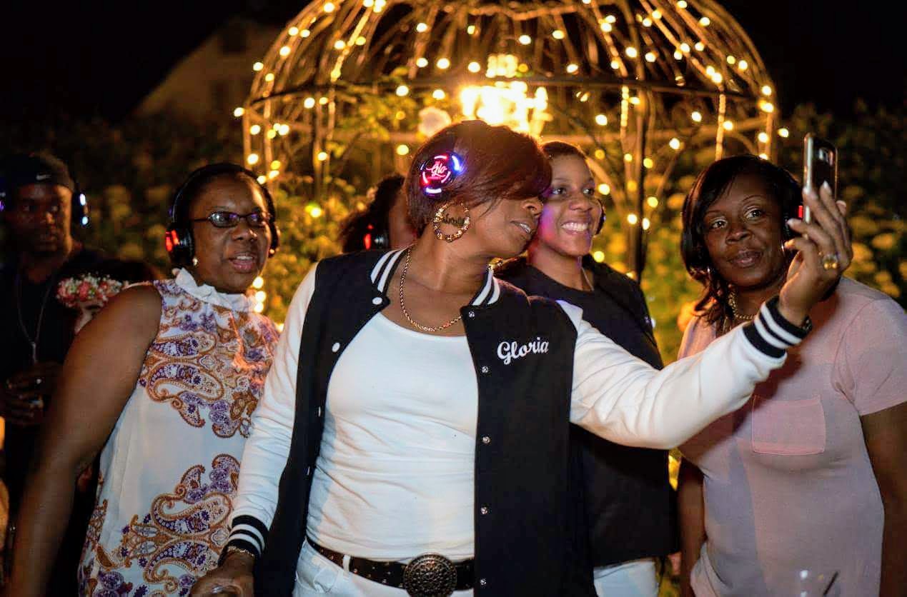 Gloria D. Cassell, with short copper hair, with guests wearing headphones at the 2018 launch party for The Glo Experience.